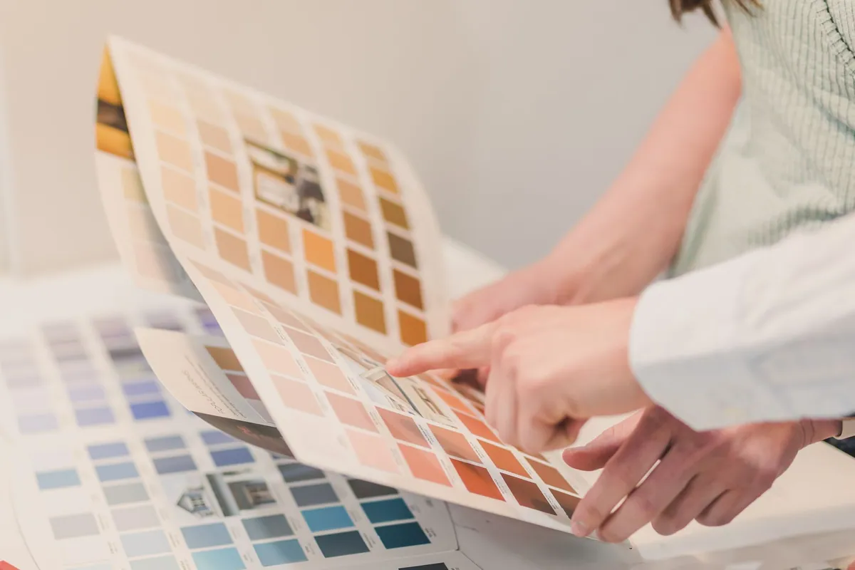 Two people comparing paint color swatches in a sample book during a color consultation